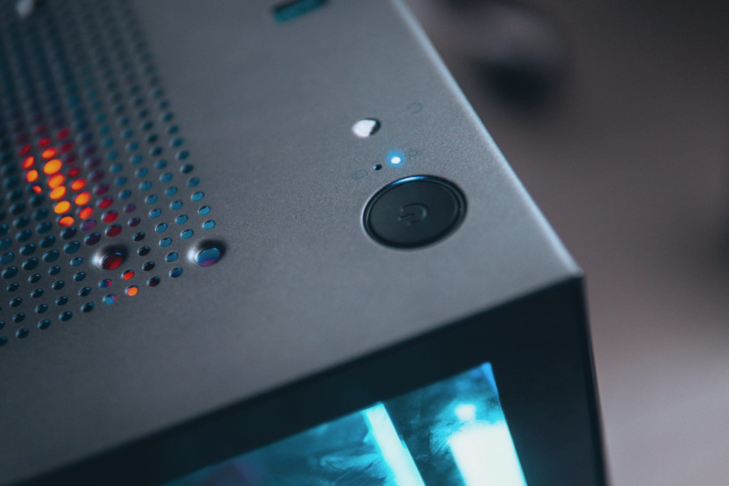 Corner of a dark grey computer case with a power button, vent holes and a cyan glow.