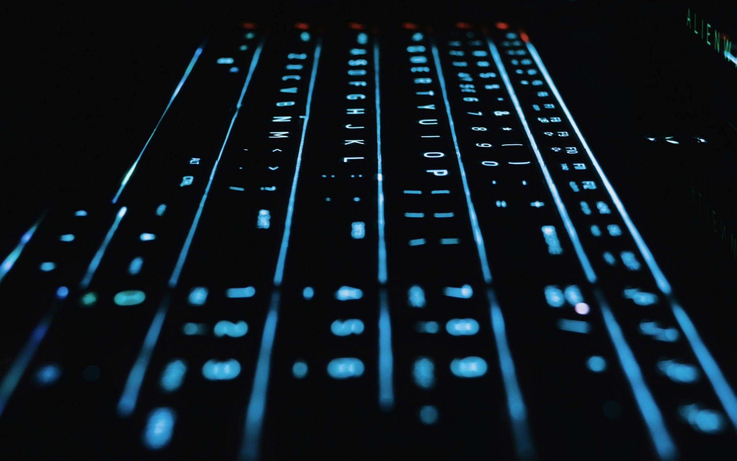 A mechanical keyboard with blue-cyan backlight shot at a low angle in the dark.